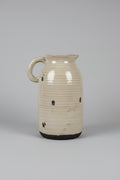 Rustic ceramic pitcher vase with off-white glaze and dark unglazed base on a wooden surface