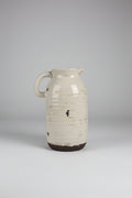 Ribbed ceramic pitcher vase with off-white glaze and dark unglazed base on a wooden surface