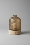 Smoked amber textured glass vase with ribbed wooden base on a wooden surface