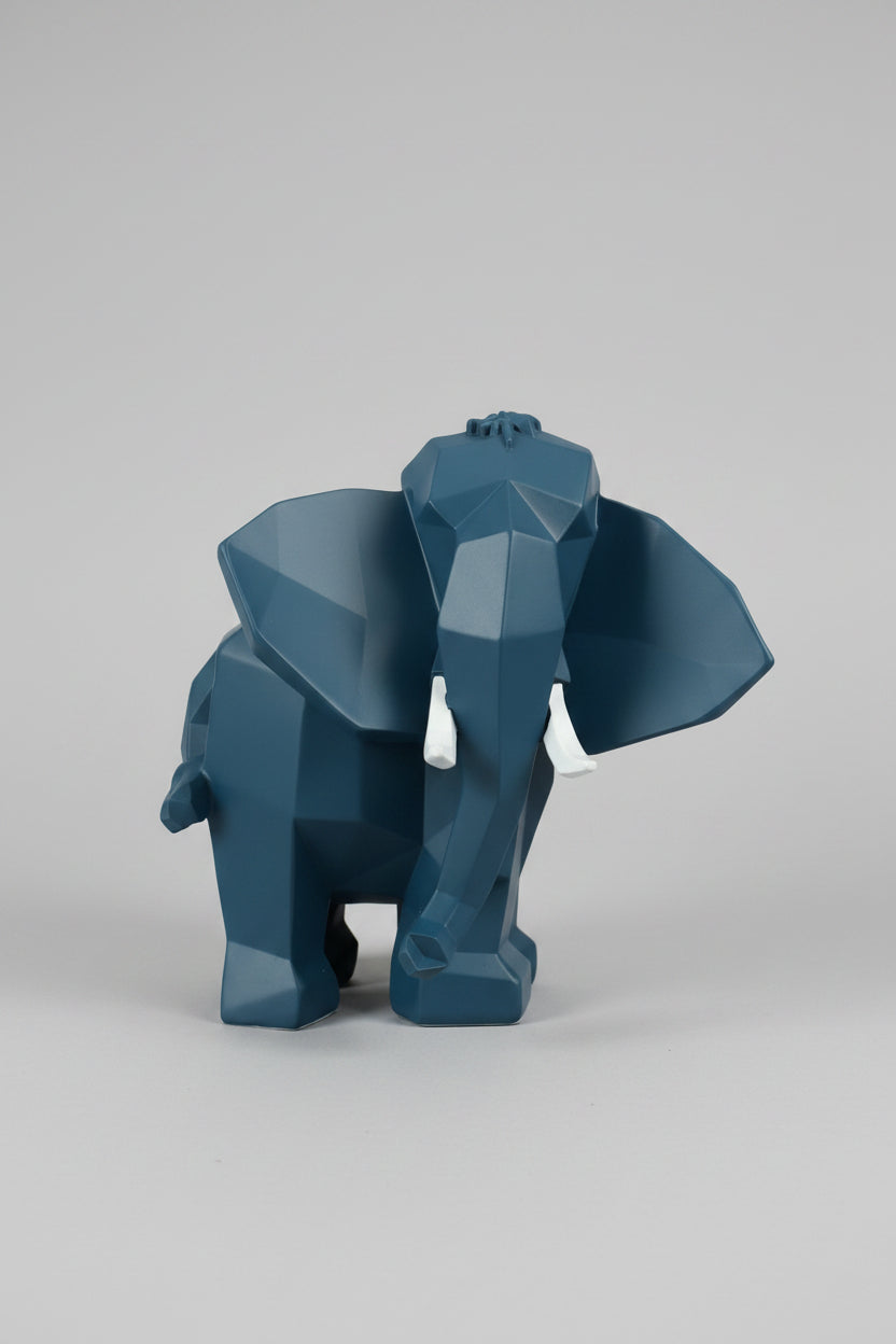 Low-poly geometric elephant sculpture in deep slate navy with white tusks on a wooden surface