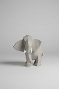 Low-poly geometric elephant sculpture in cool concrete grey with white tusks on a wooden surface
