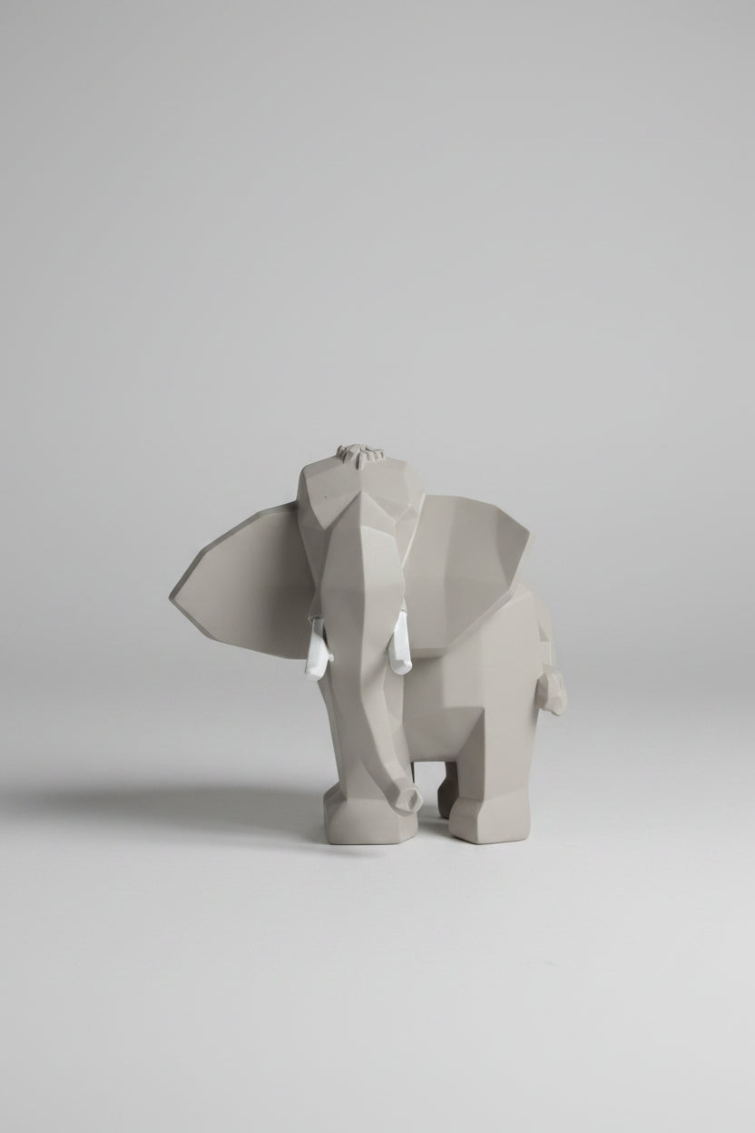 Low-poly geometric elephant sculpture in cool concrete grey with white tusks on a wooden surface
