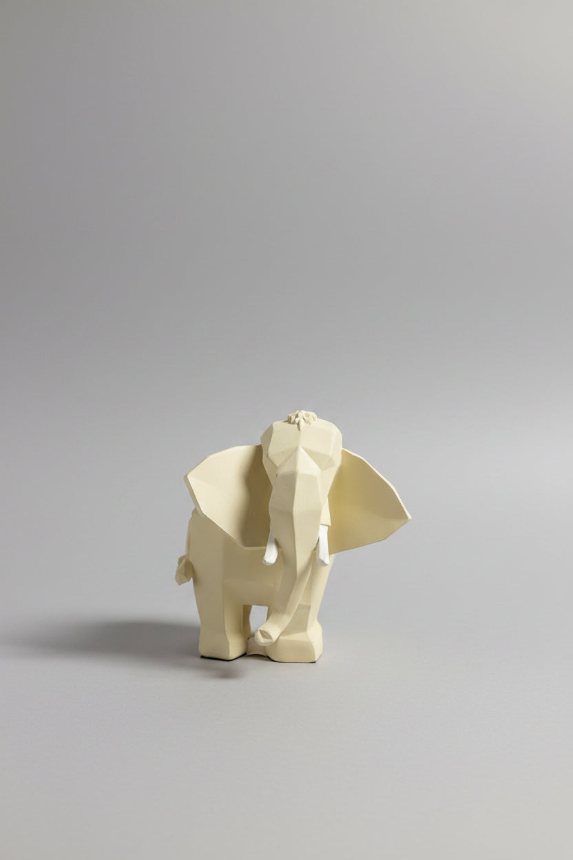 Low-poly geometric elephant sculpture in warm ivory cream with white tusks on a wooden surface