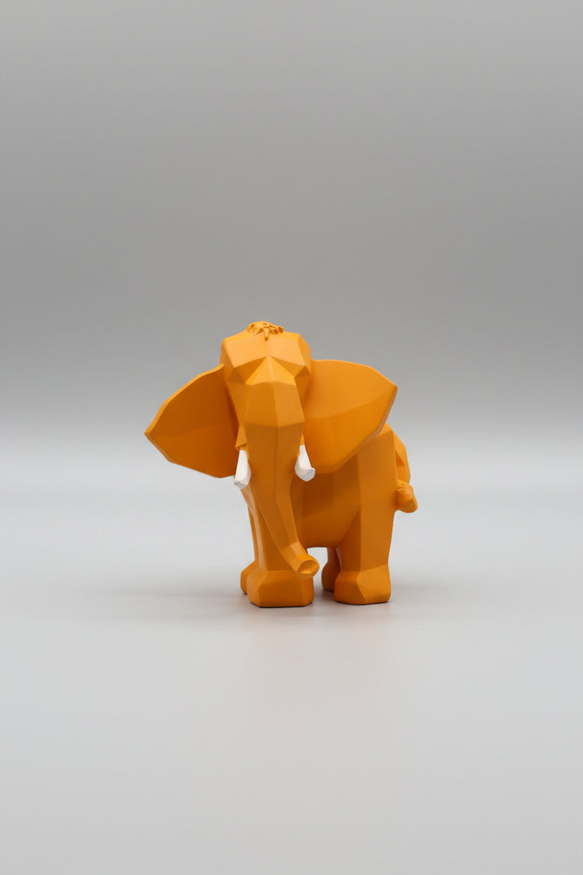 Low-poly geometric elephant sculpture in warm amber mustard yellow with white tusks on a wooden surface