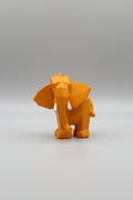 Low-poly geometric elephant sculpture in warm amber mustard yellow with white tusks on a wooden surface